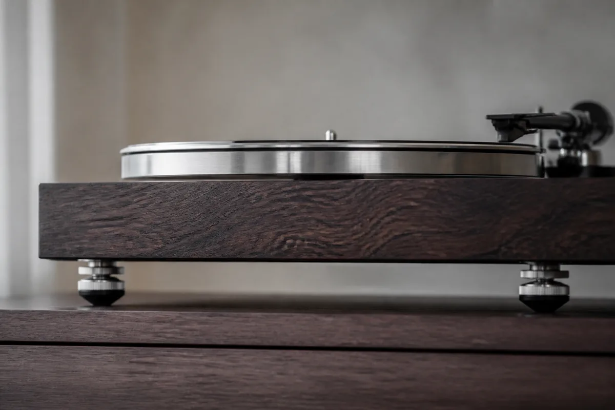Détail du plateau et du socle d&rsquo;une platine vinyle posée sur un meuble en bois